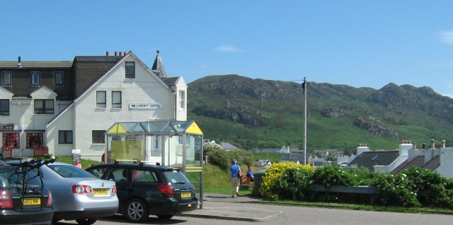 gairloch in the sunshine, a white building and car park with hills in the background